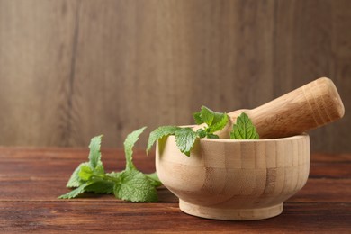 Photo of Fresh lemon balm leaves, pestle and mortar on wooden table, closeup