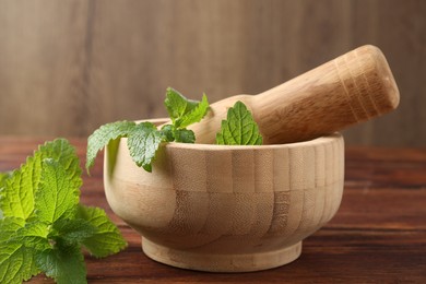 Photo of Fresh lemon balm leaves, pestle and mortar on wooden table, closeup