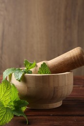 Photo of Fresh lemon balm leaves, pestle and mortar on wooden table, closeup. Space for text