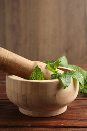 Photo of Fresh lemon balm leaves, pestle and mortar on wooden table, closeup. Space for text