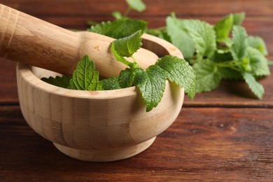 Photo of Fresh lemon balm leaves, pestle and mortar on wooden table, closeup