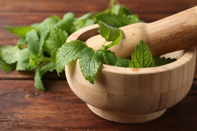 Photo of Fresh lemon balm leaves, pestle and mortar on wooden table, closeup