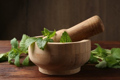 Photo of Fresh lemon balm leaves, pestle and mortar on wooden table, closeup
