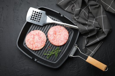 Photo of Fresh raw patties for burger and spices in frying pan on black table, top view