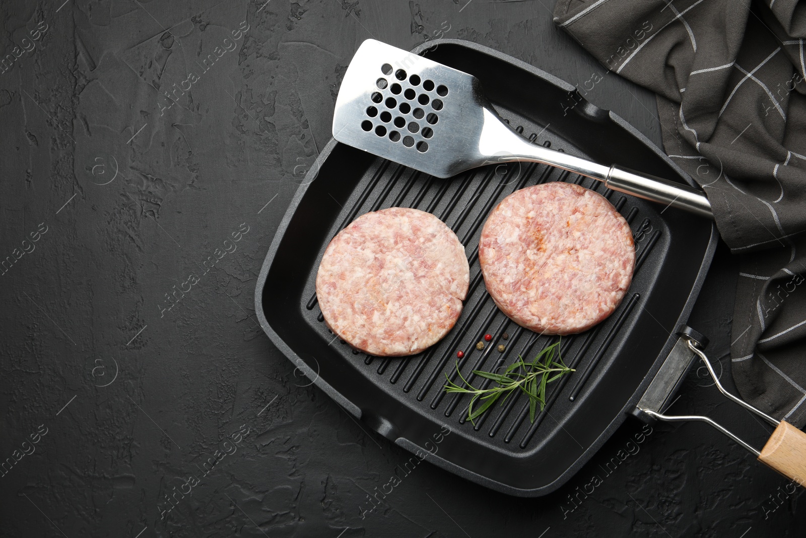 Fresh raw patties for burger and spices in frying pan on black table, top view. Space for text Photo of Fresh raw patties for burger and spices in frying pan on black table, top view. Space for text