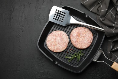 Photo of Fresh raw patties for burger and spices in frying pan on black table, top view. Space for text