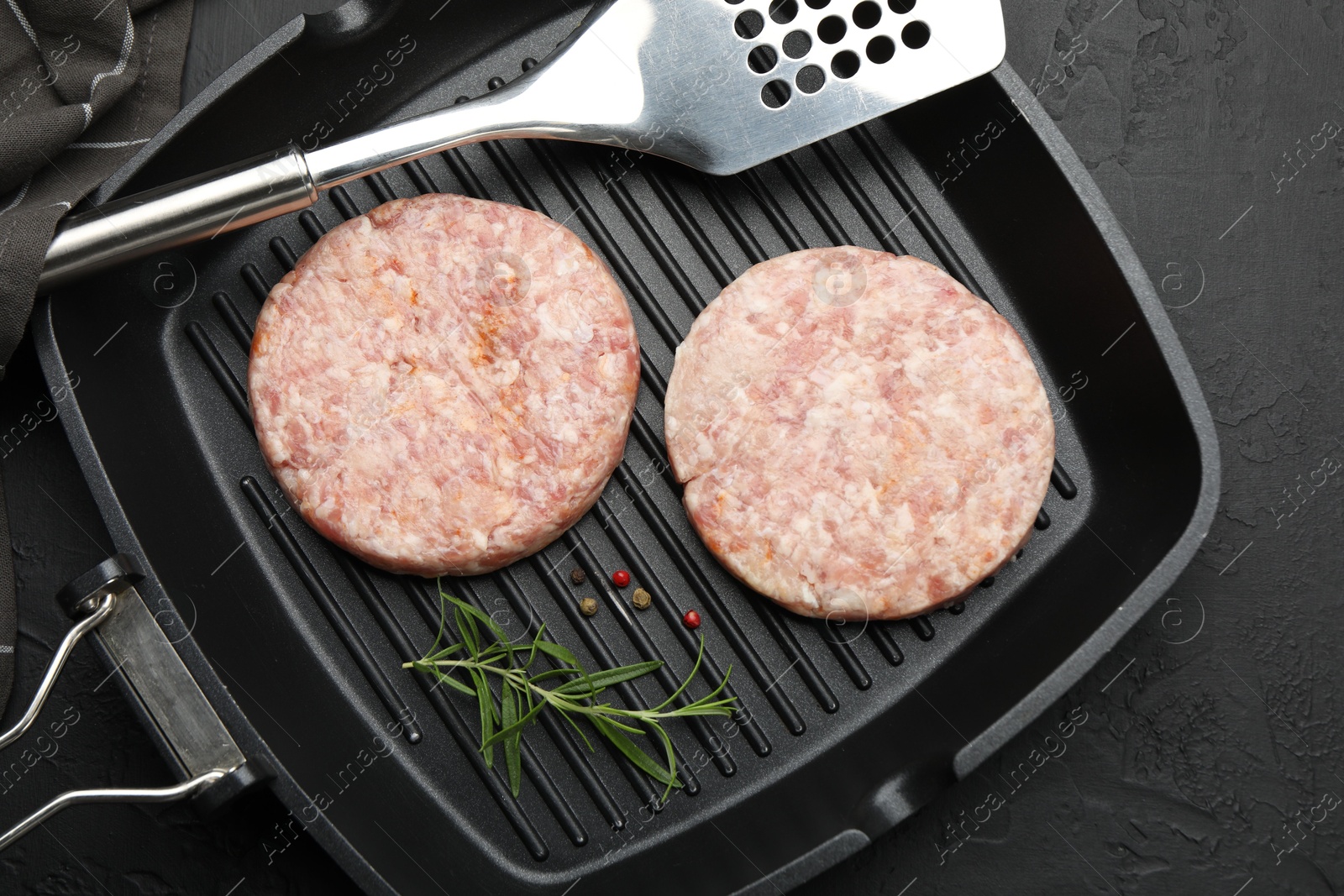 Fresh raw patties for burger and spices in frying pan on black table, top view Photo of Fresh raw patties for burger and spices in frying pan on black table, top view