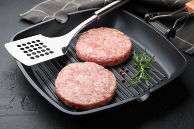 Photo of Fresh raw patties for burger and spices in frying pan on black table, closeup