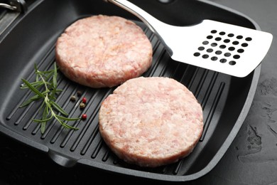 Photo of Fresh raw patties for burger and spices in frying pan on black table, closeup