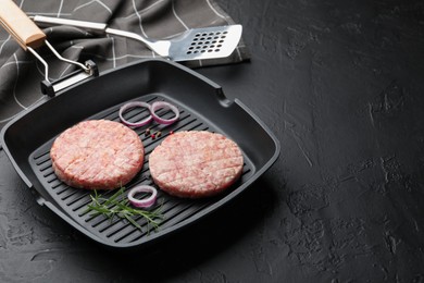 Photo of Fresh raw patties for burger and spices in frying pan on black table, closeup. Space for text