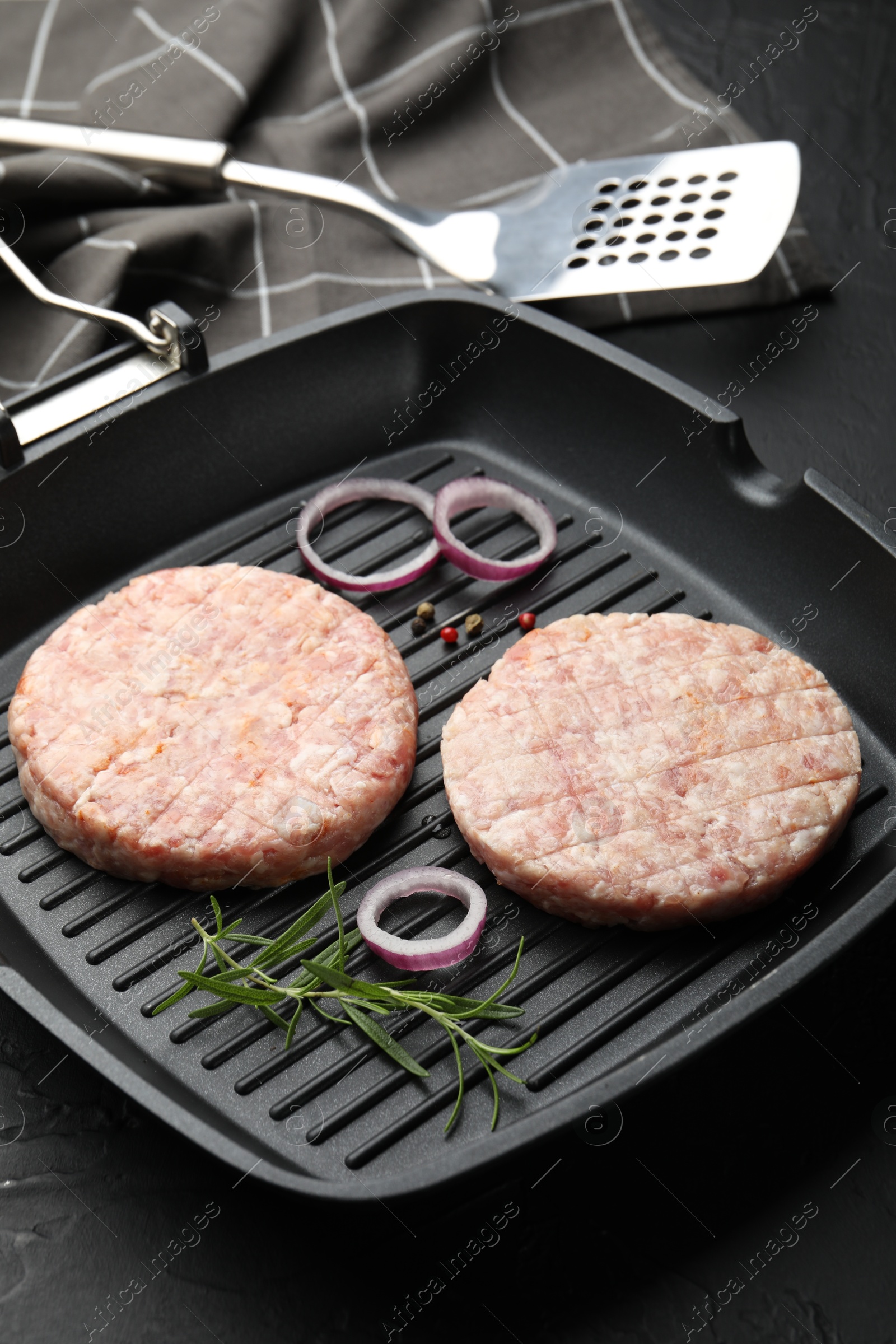 Fresh raw patties for burger and spices in frying pan on black table, closeup Photo of Fresh raw patties for burger and spices in frying pan on black table, closeup