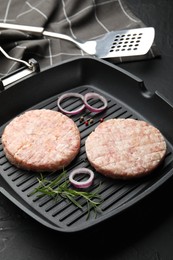 Photo of Fresh raw patties for burger and spices in frying pan on black table, closeup