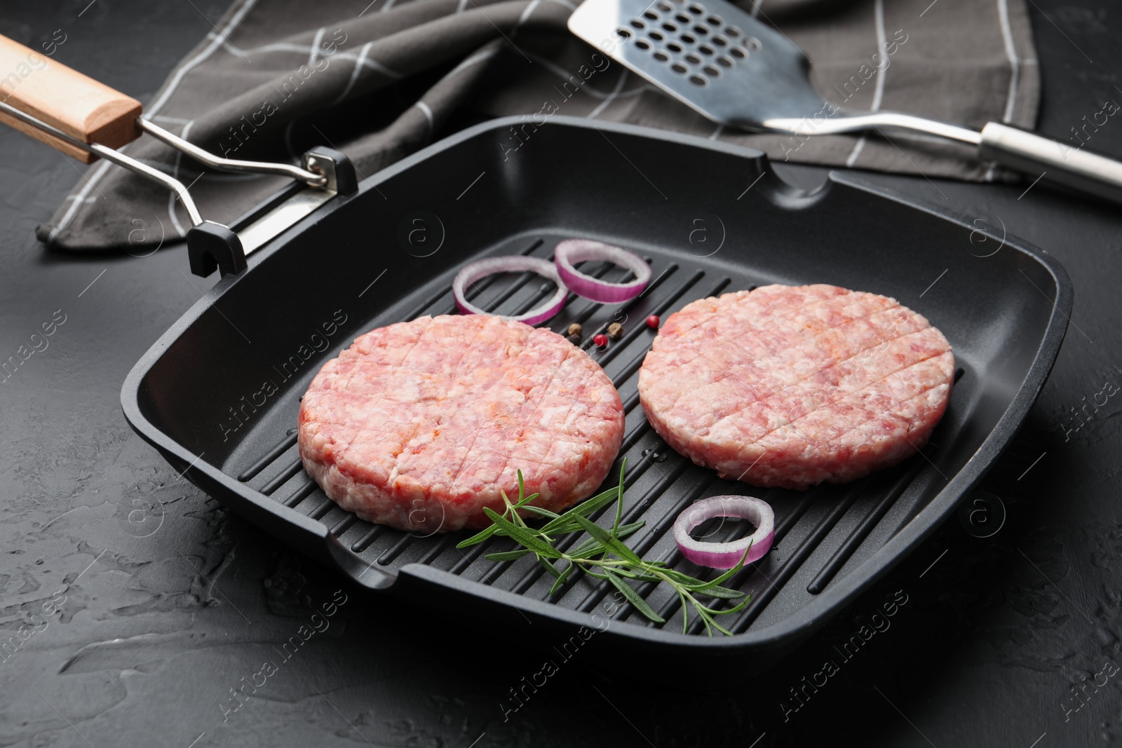 Fresh raw patties for burger and spices in frying pan on black table, closeup Photo of Fresh raw patties for burger and spices in frying pan on black table, closeup