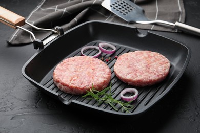 Photo of Fresh raw patties for burger and spices in frying pan on black table, closeup