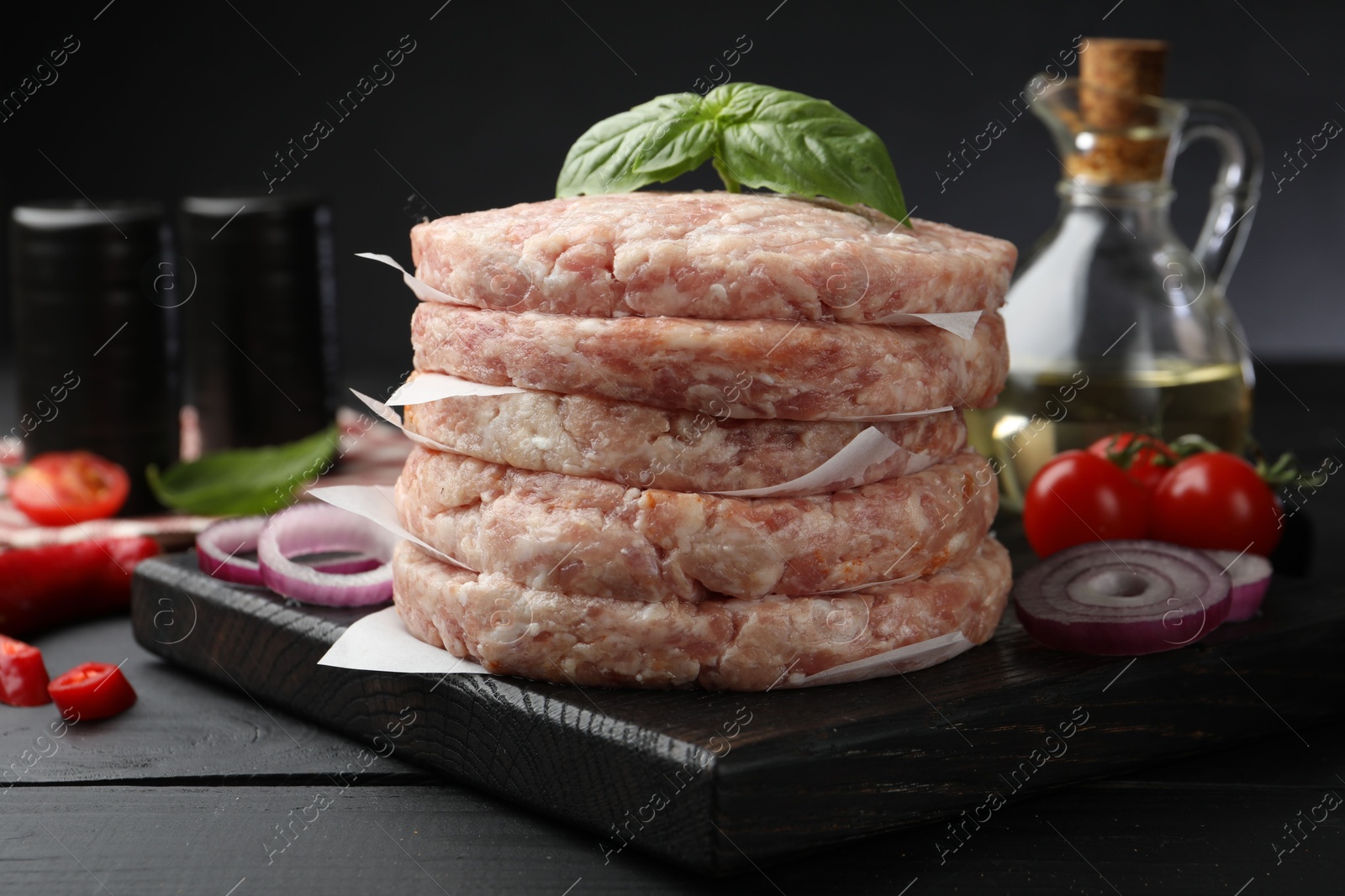 Fresh raw patties for burger, spices and tomatoes on black wooden table, closeup Photo of Fresh raw patties for burger, spices and tomatoes on black wooden table, closeup