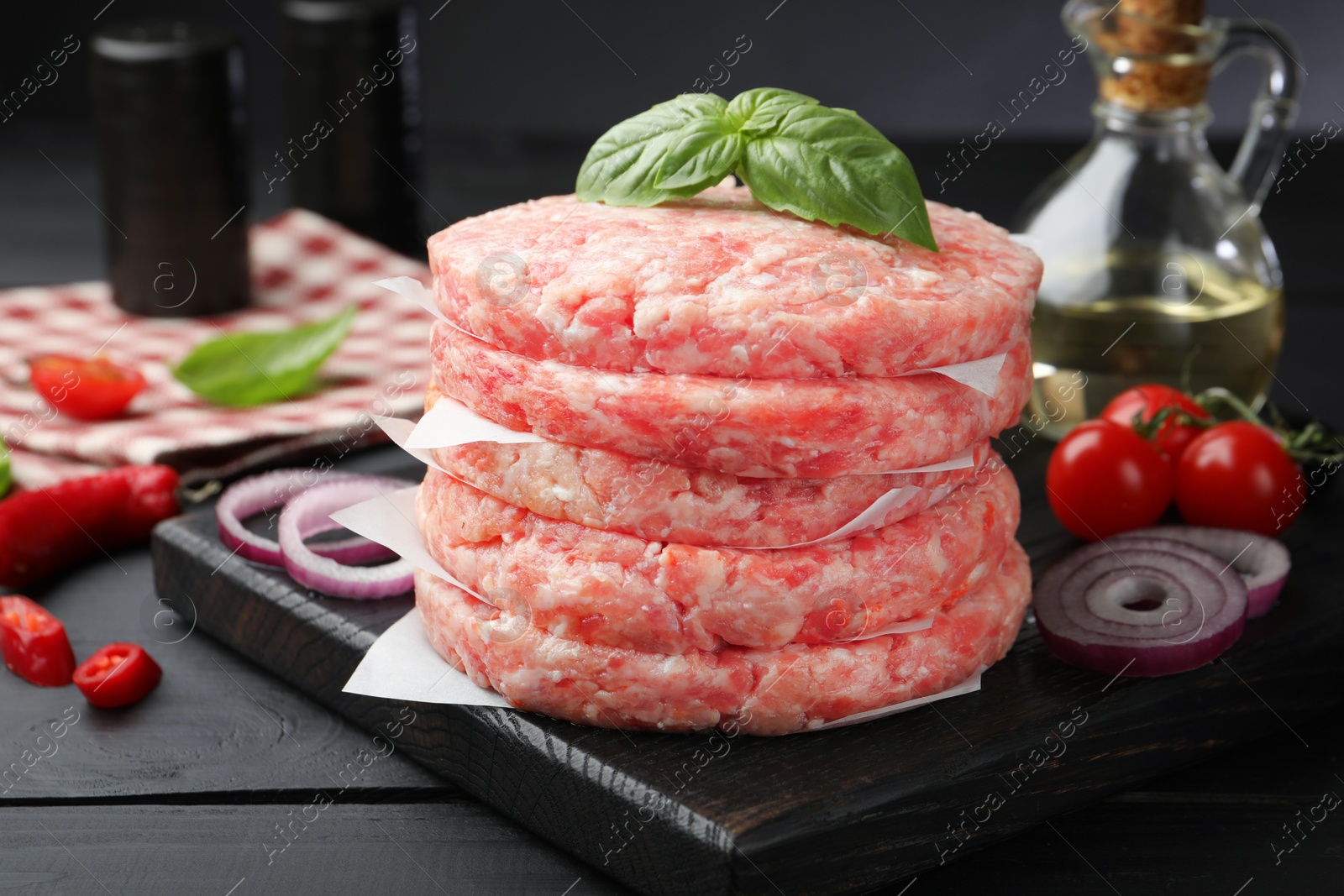 Fresh raw patties for burger, spices and tomatoes on black wooden table, closeup Photo of Fresh raw patties for burger, spices and tomatoes on black wooden table, closeup