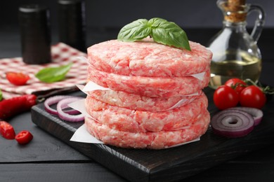 Photo of Fresh raw patties for burger, spices and tomatoes on black wooden table, closeup
