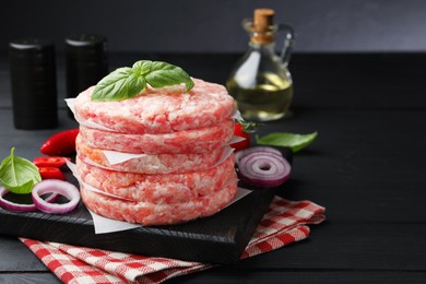 Photo of Fresh raw patties for burger and spices on black wooden table, closeup. Space for text