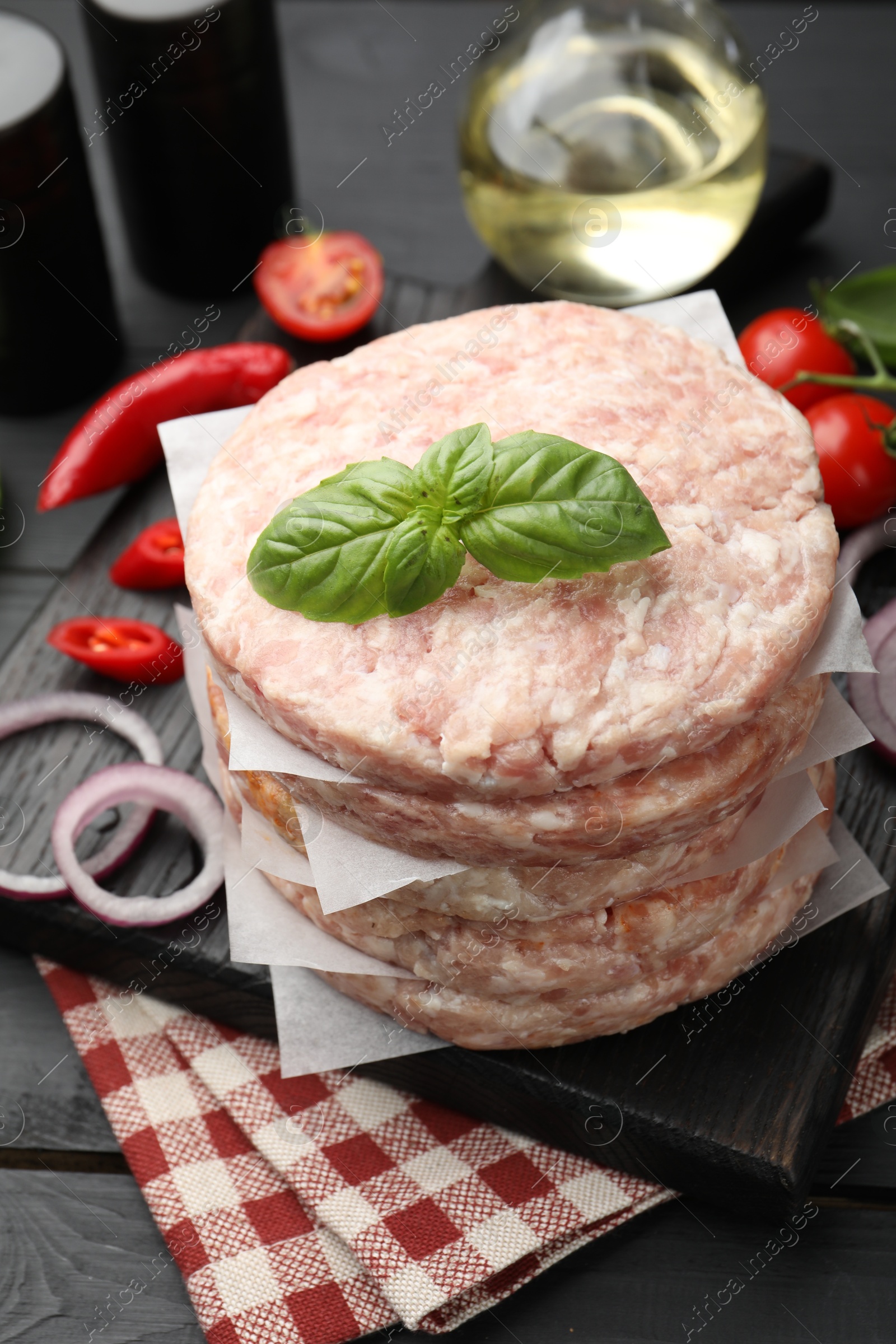 Fresh raw patties for burger, spices and tomatoes on black wooden table, closeup Photo of Fresh raw patties for burger, spices and tomatoes on black wooden table, closeup
