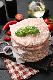 Photo of Fresh raw patties for burger, spices and tomatoes on black wooden table, closeup