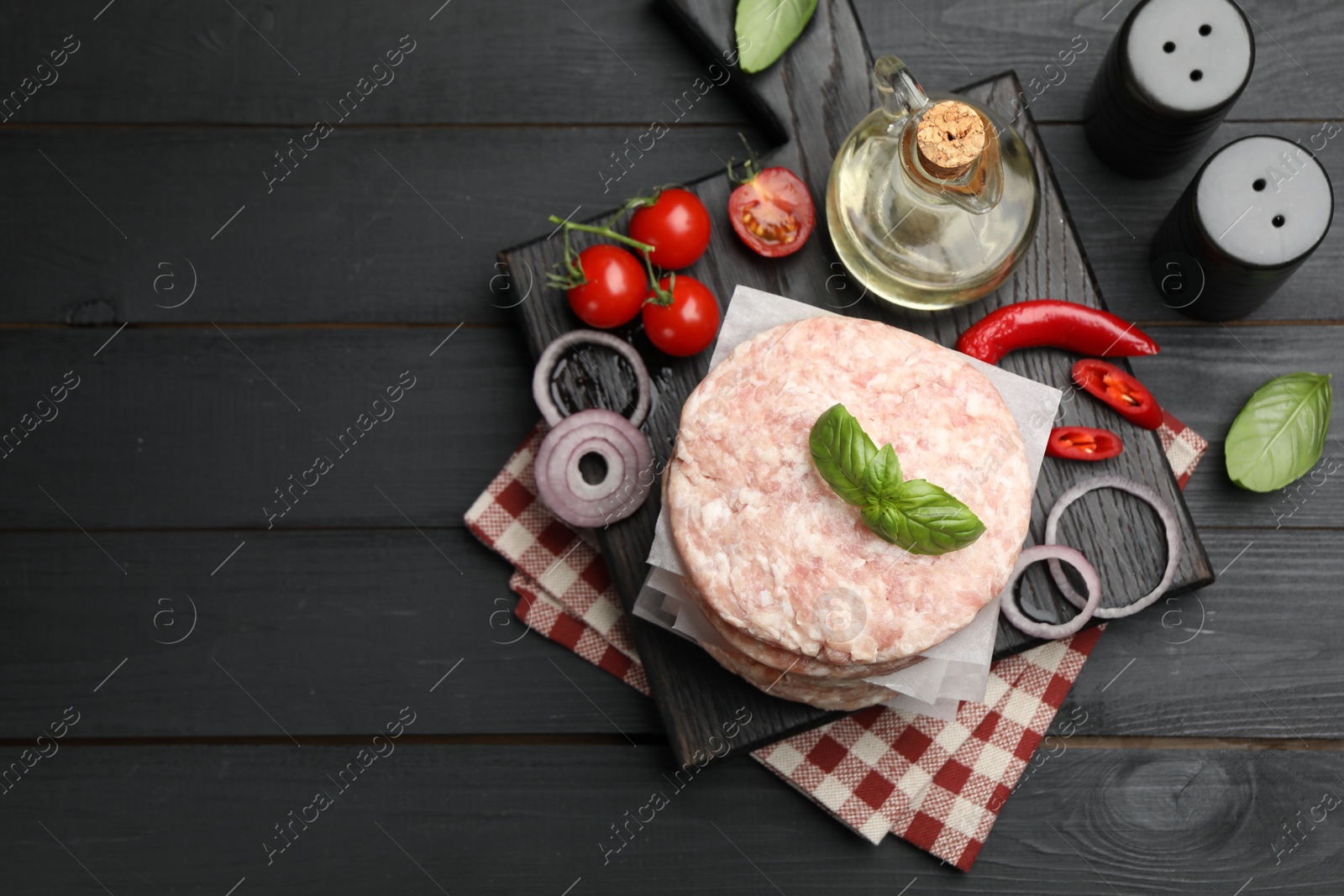 Fresh raw patties for burger, spices and tomatoes on black wooden table, flat lay. Space for text Photo of Fresh raw patties for burger, spices and tomatoes on black wooden table, flat lay. Space for text