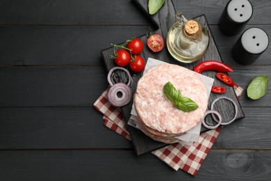 Photo of Fresh raw patties for burger, spices and tomatoes on black wooden table, flat lay. Space for text