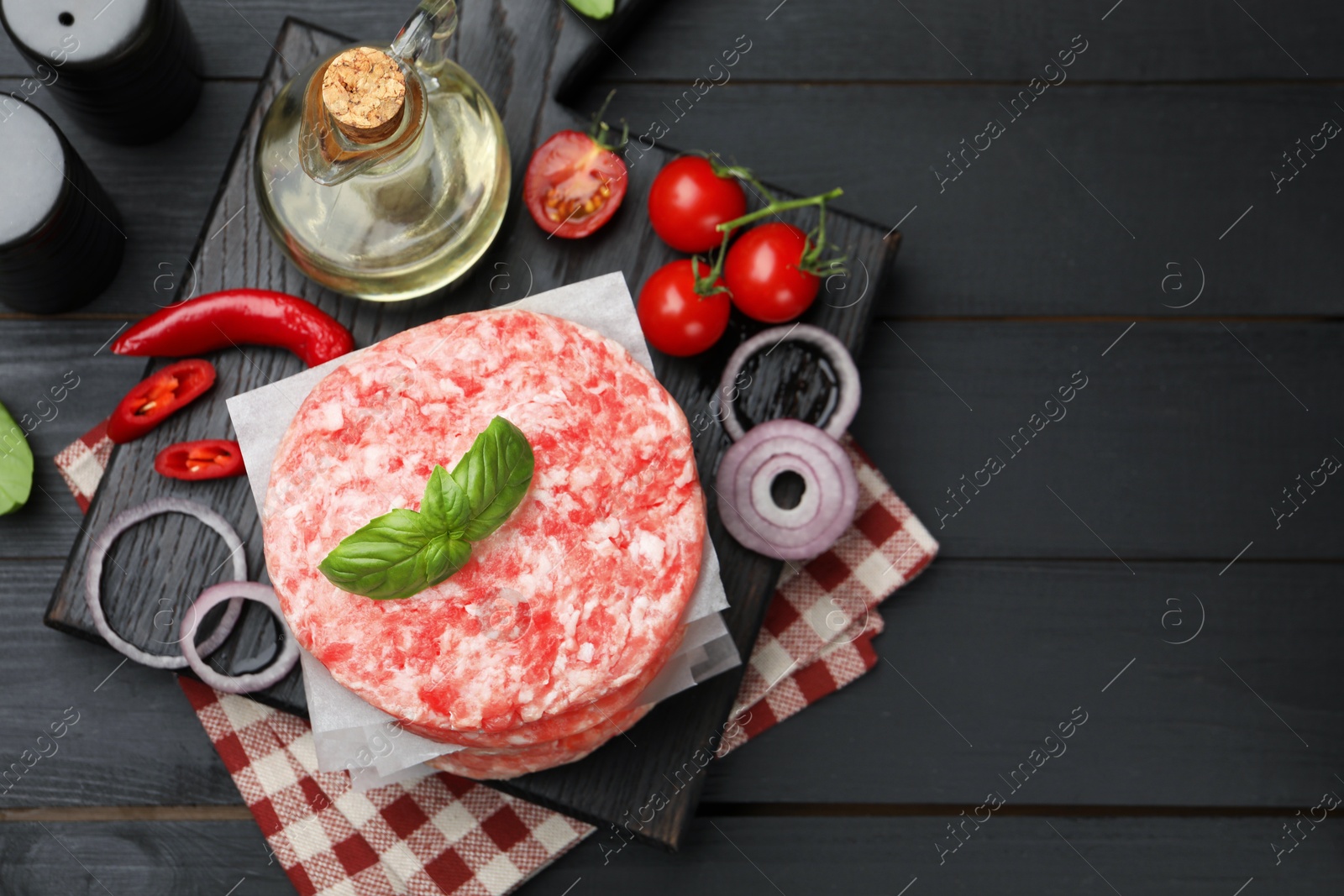 Fresh raw patties for burger, spices and tomatoes on black wooden table, flat lay. Space for text Photo of Fresh raw patties for burger, spices and tomatoes on black wooden table, flat lay. Space for text