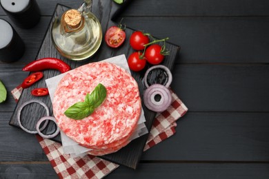 Photo of Fresh raw patties for burger, spices and tomatoes on black wooden table, flat lay. Space for text