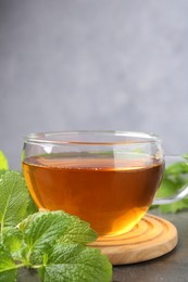 Photo of Aromatic lemon balm tea in glass cup and fresh leaves on gray table, closeup. Space for text