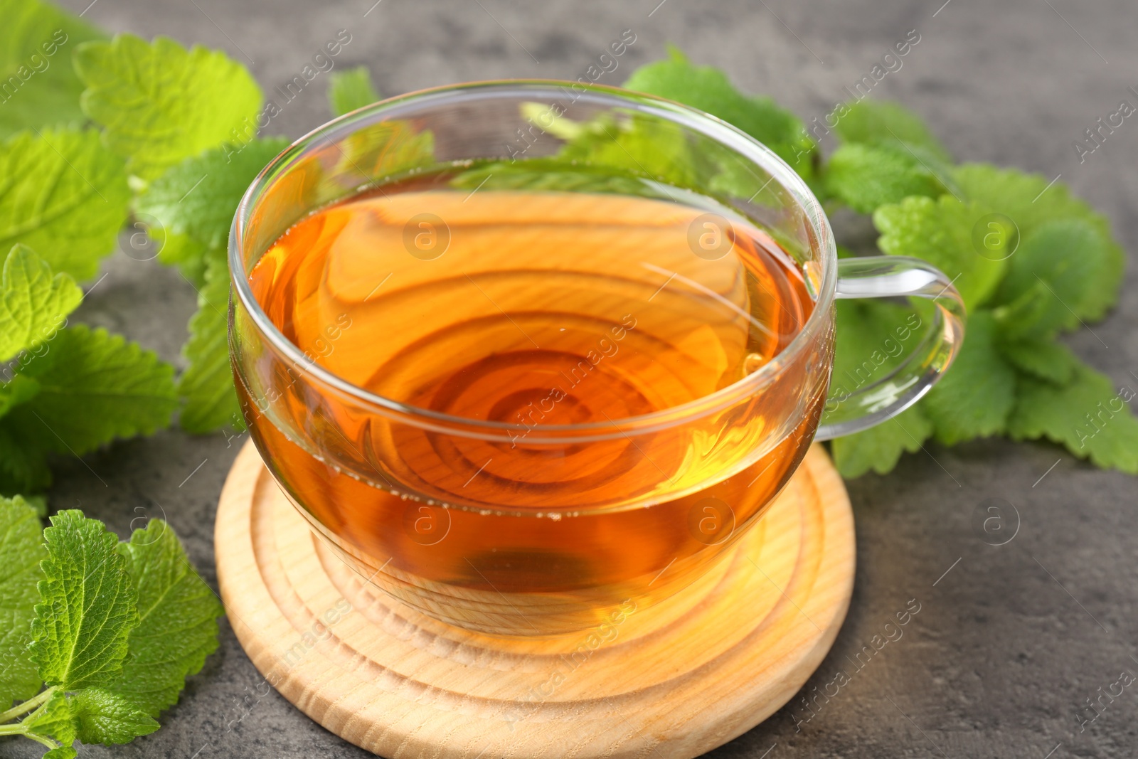 Aromatic lemon balm tea in glass cup and fresh leaves on gray table, closeup Photo of Aromatic lemon balm tea in glass cup and fresh leaves on gray table, closeup