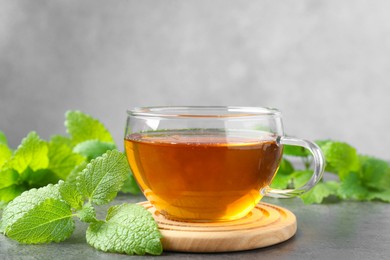 Photo of Aromatic lemon balm tea in glass cup and fresh leaves on gray textured table