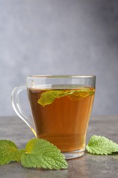 Photo of Aromatic lemon balm tea in glass cup and fresh leaves on gray textured table