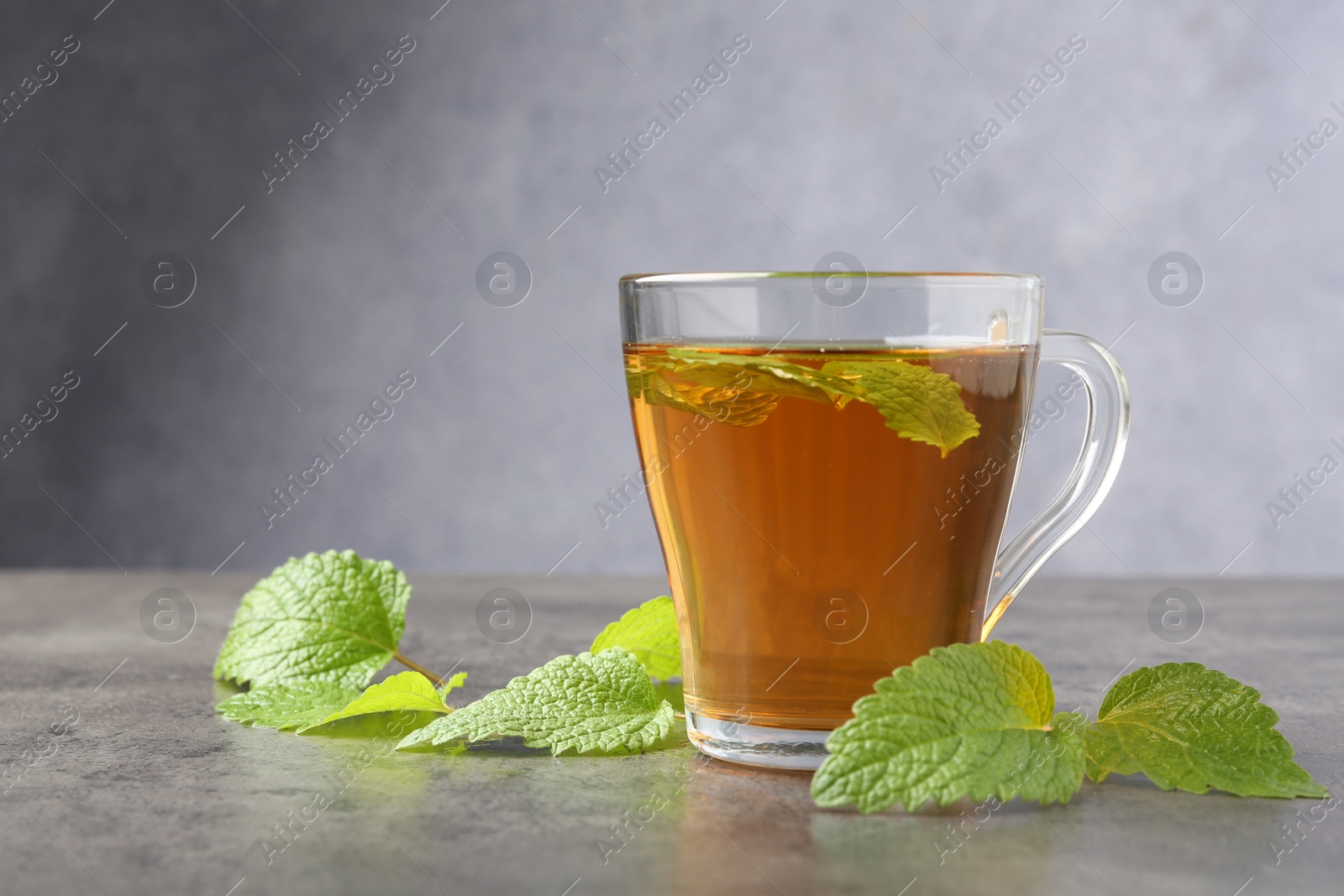 Aromatic lemon balm tea in glass cup and fresh leaves on gray textured table, space for text Photo of Aromatic lemon balm tea in glass cup and fresh leaves on gray textured table, space for text