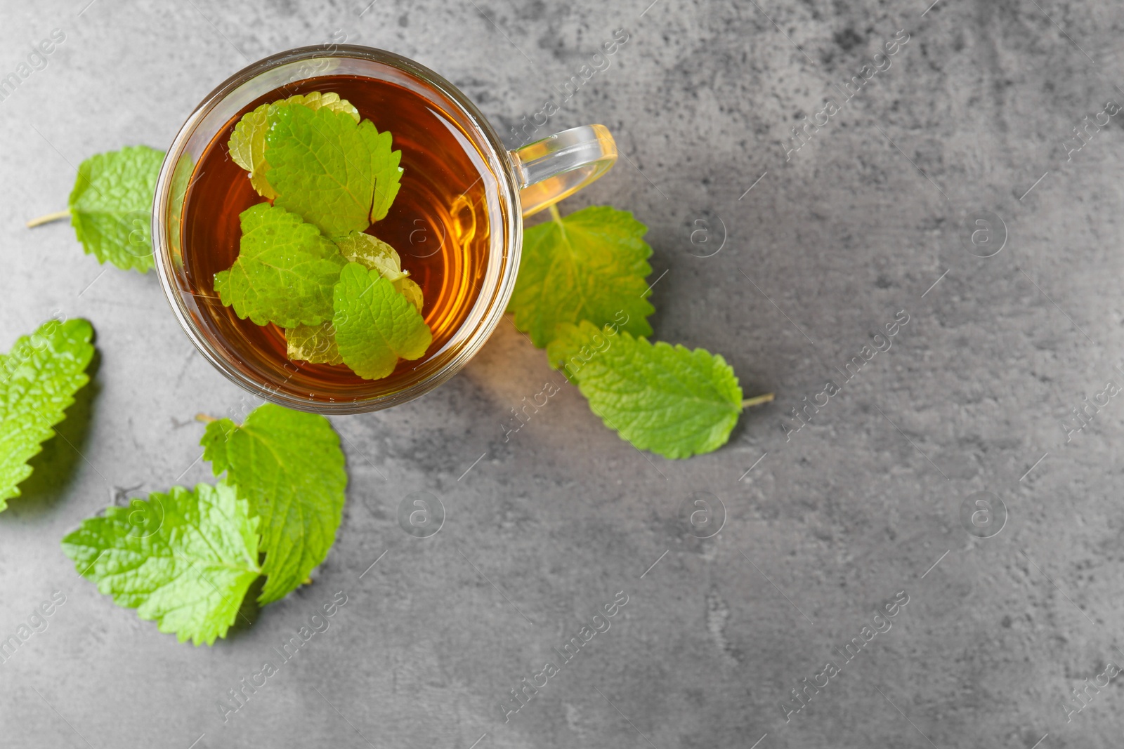 Aromatic lemon balm tea in glass cup and fresh leaves on gray textured table, flat lay. Space for text Photo of Aromatic lemon balm tea in glass cup and fresh leaves on gray textured table, flat lay. Space for text