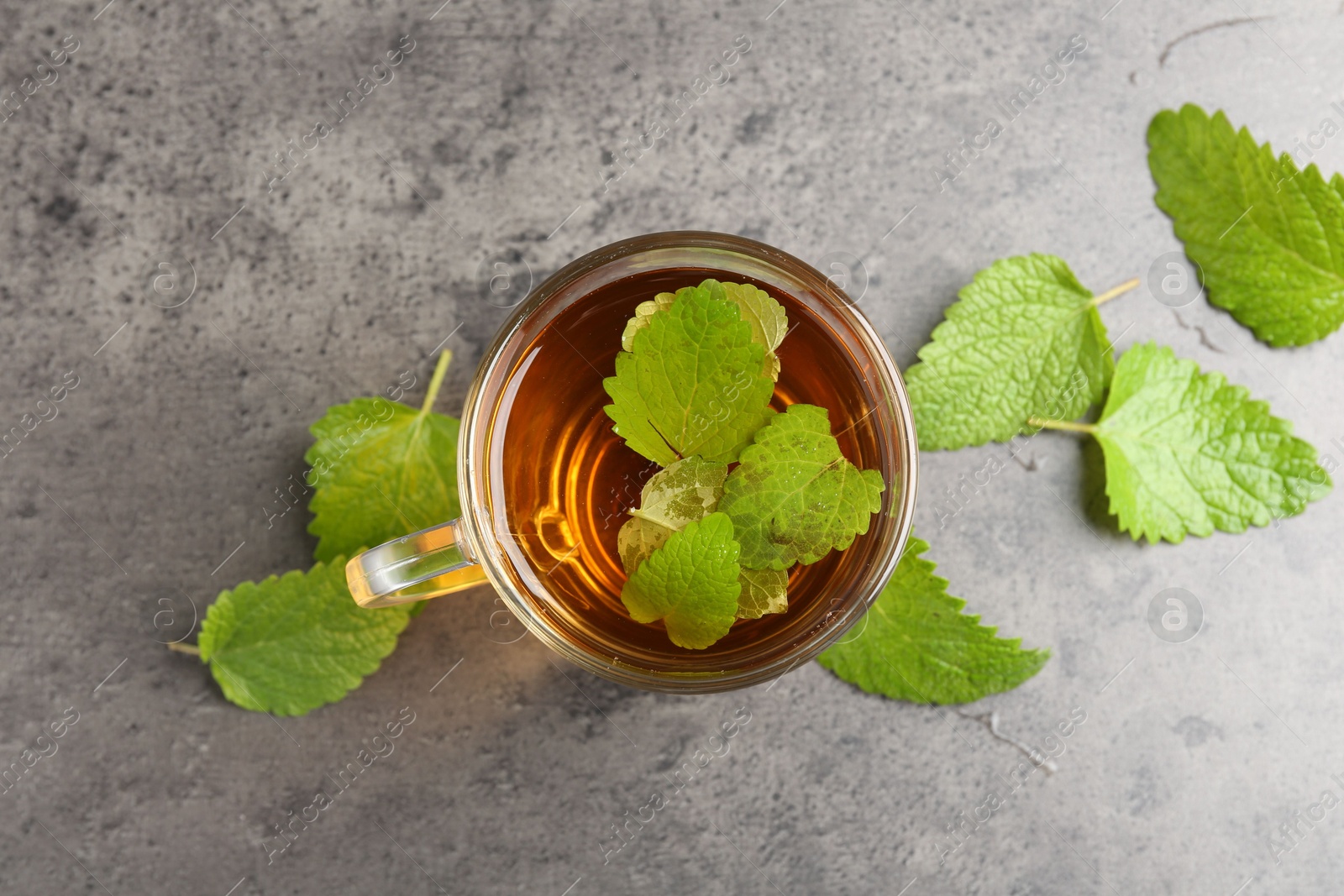 Aromatic lemon balm tea in glass cup and fresh leaves on gray textured table, flat lay Photo of Aromatic lemon balm tea in glass cup and fresh leaves on gray textured table, flat lay