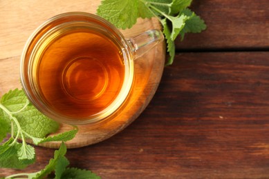Photo of Aromatic lemon balm tea in glass cup and fresh leaves on wooden table, top view. Space for text