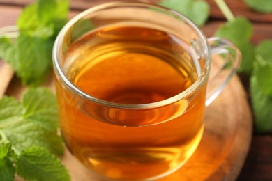 Photo of Aromatic lemon balm tea in glass cup and fresh leaves on table, closeup