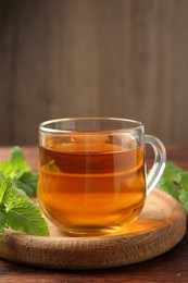 Photo of Aromatic lemon balm tea in glass cup and fresh leaves on wooden table