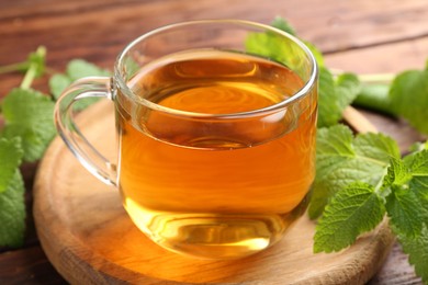 Photo of Aromatic lemon balm tea in glass cup and fresh leaves on table, closeup