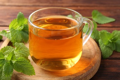 Photo of Aromatic lemon balm tea in glass cup and fresh leaves on table, closeup
