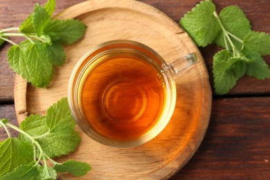 Photo of Aromatic lemon balm tea in glass cup and fresh leaves on wooden table, flat lay