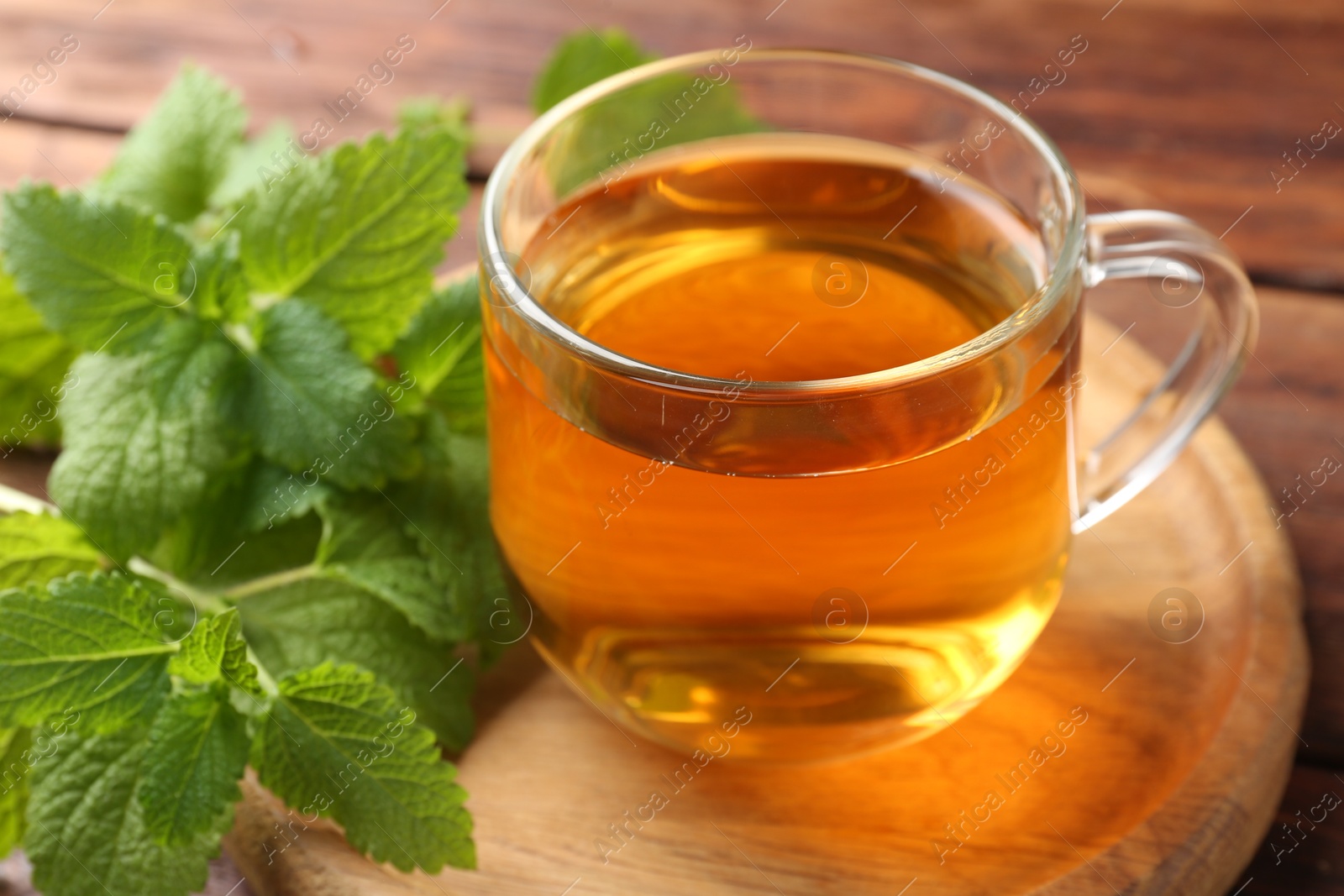 Aromatic lemon balm tea in glass cup and fresh leaves on table, closeup Photo of Aromatic lemon balm tea in glass cup and fresh leaves on table, closeup
