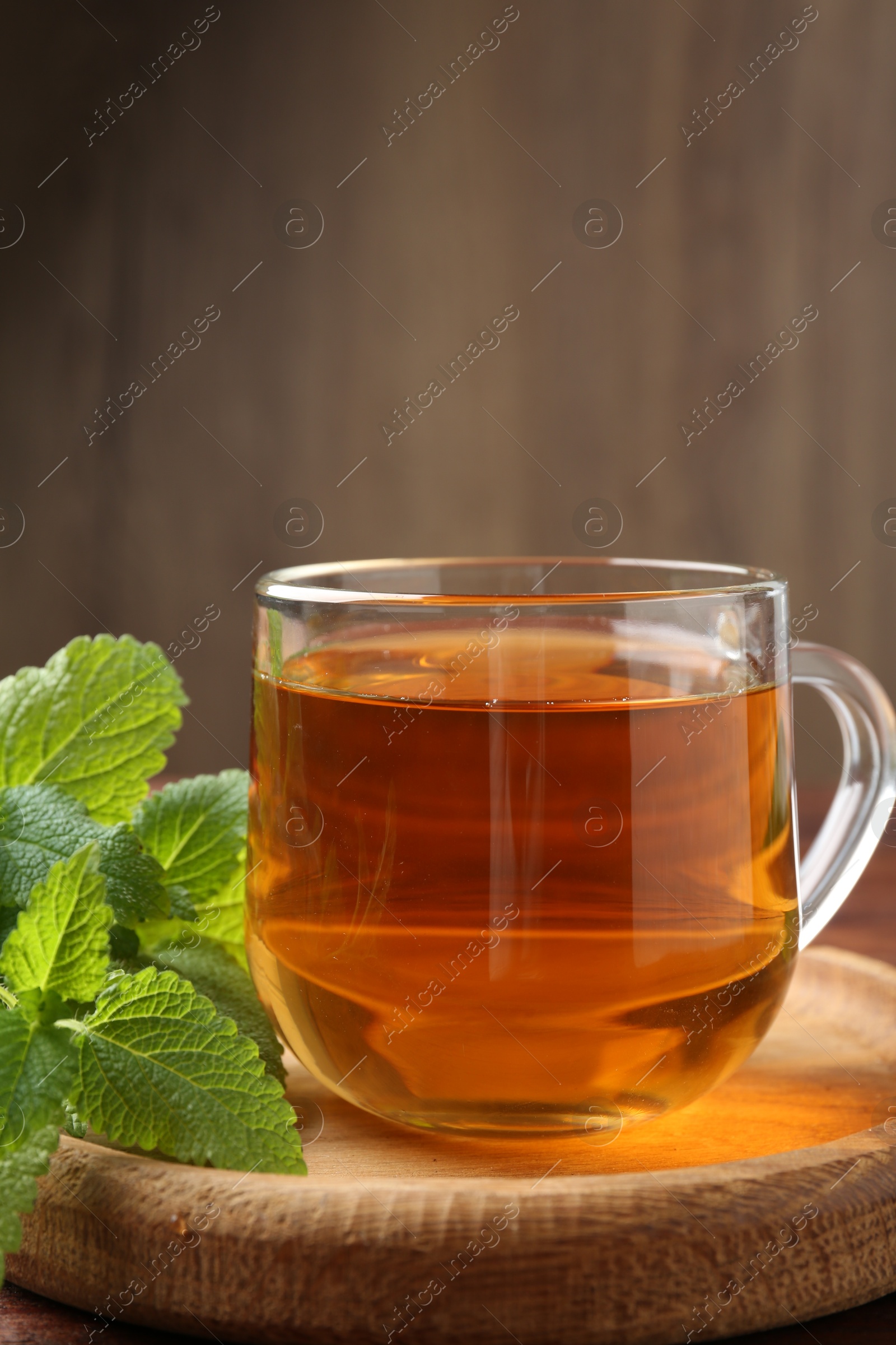 Aromatic lemon balm tea in glass cup and fresh leaves on wooden table Photo of Aromatic lemon balm tea in glass cup and fresh leaves on wooden table