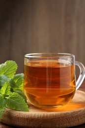 Photo of Aromatic lemon balm tea in glass cup and fresh leaves on wooden table