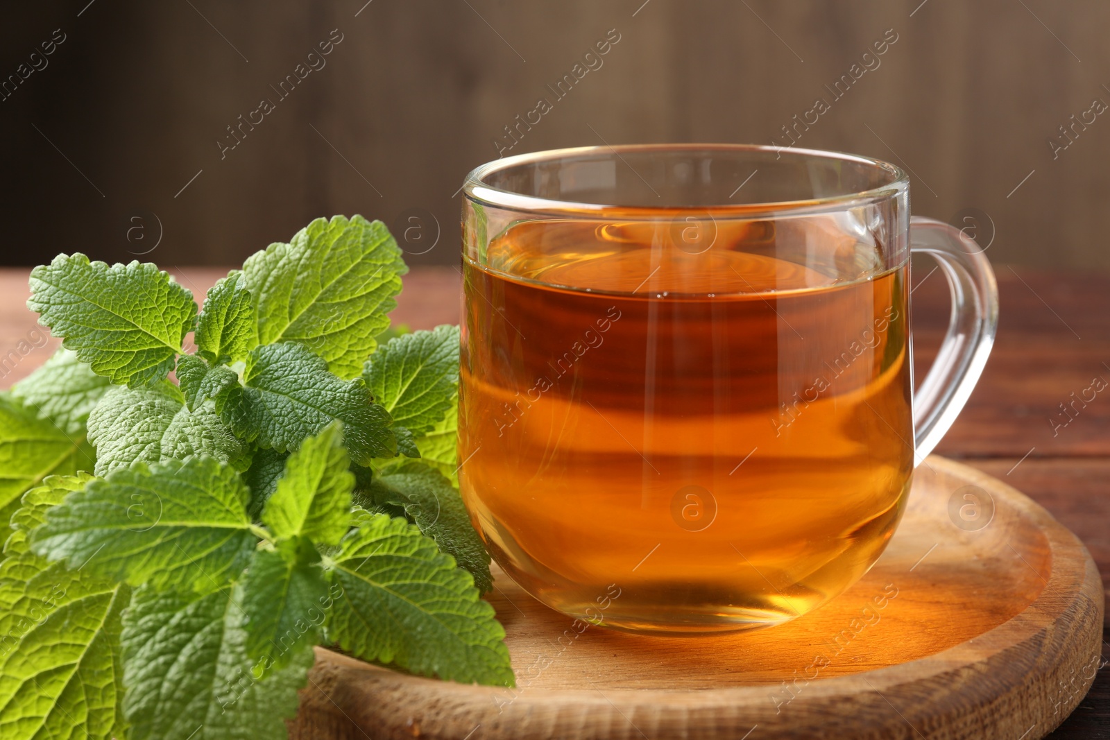 Aromatic lemon balm tea in glass cup and fresh leaves on table, closeup Photo of Aromatic lemon balm tea in glass cup and fresh leaves on table, closeup