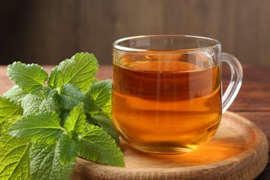 Photo of Aromatic lemon balm tea in glass cup and fresh leaves on table, closeup