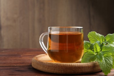 Photo of Aromatic lemon balm tea in glass cup and fresh leaves on wooden table, space for text