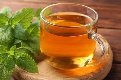 Photo of Aromatic lemon balm tea in glass cup and fresh leaves on table, closeup