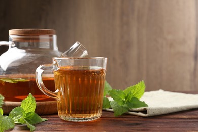 Photo of Aromatic lemon balm tea in glass cup, teapot and fresh leaves on wooden table, space for text