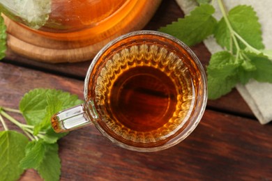 Photo of Aromatic lemon balm tea in glass cup, teapot and fresh leaves on wooden table, flat lay